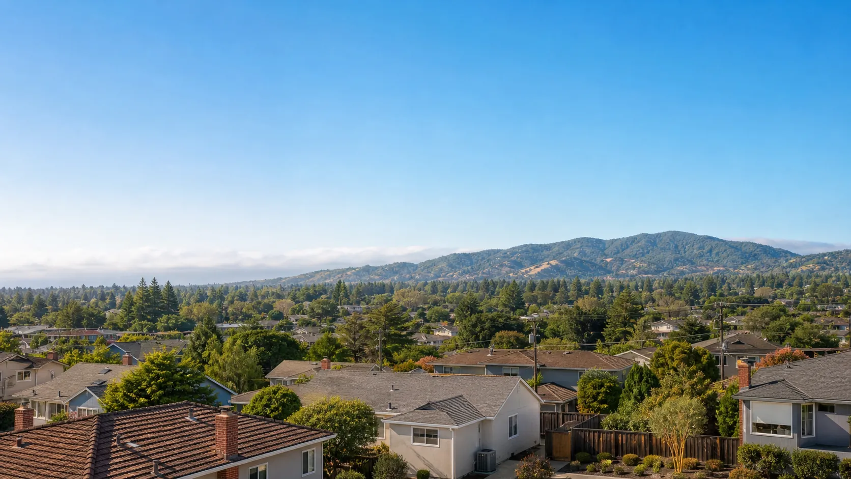 Residential Redwood City neighborhood of mid-century Peninsula homes with mature trees and the Santa Cruz foothills under a bright blue sky.